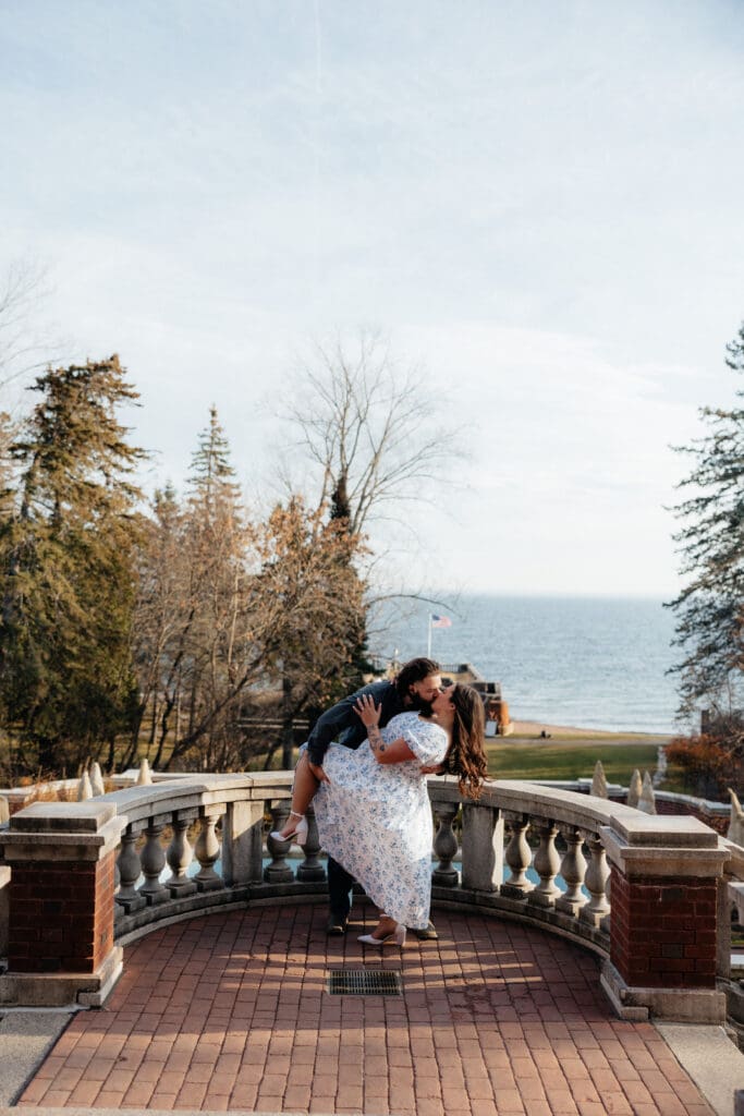 Duluth engagement session photo of a couple embracing on a terrace overlooking Lake Superior at Glensheen Mansion.