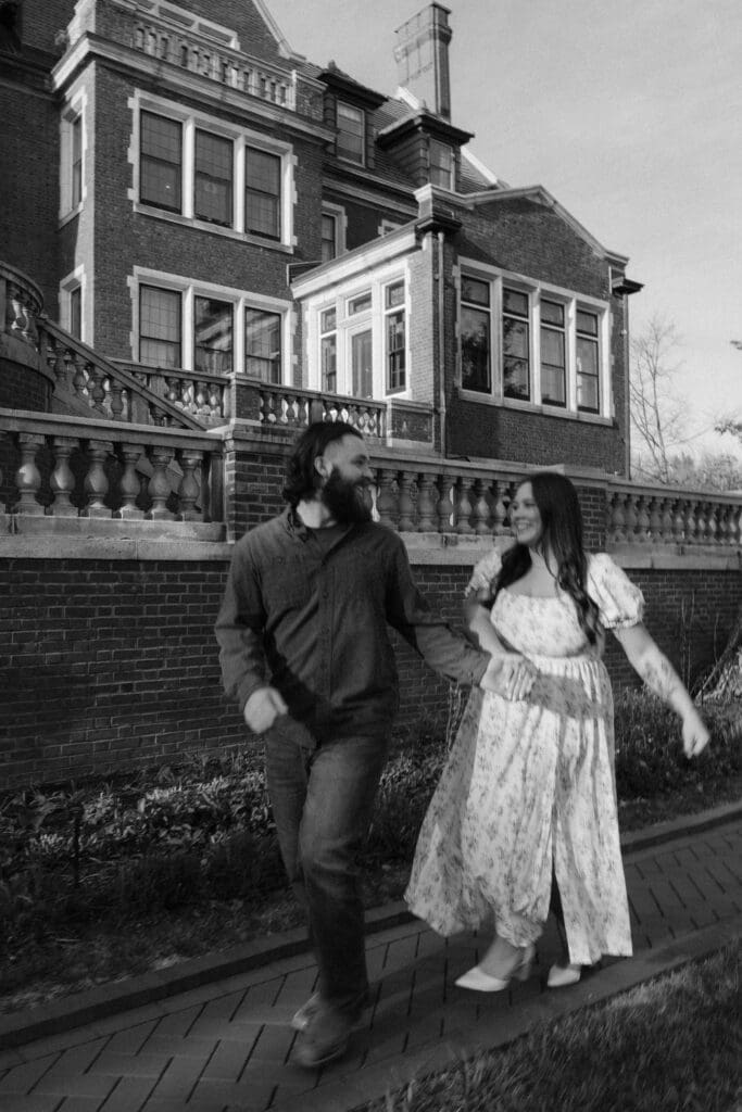 Black-and-white engagement photo of a couple walking near the grand staircase of Glensheen Mansion in Duluth, Minnesota.