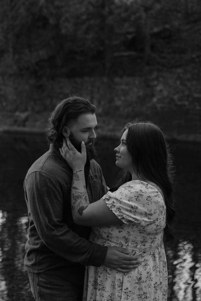 Black-and-white engagement photo of a couple embracing near a reflective pond at Glensheen Mansion in Duluth, MN.