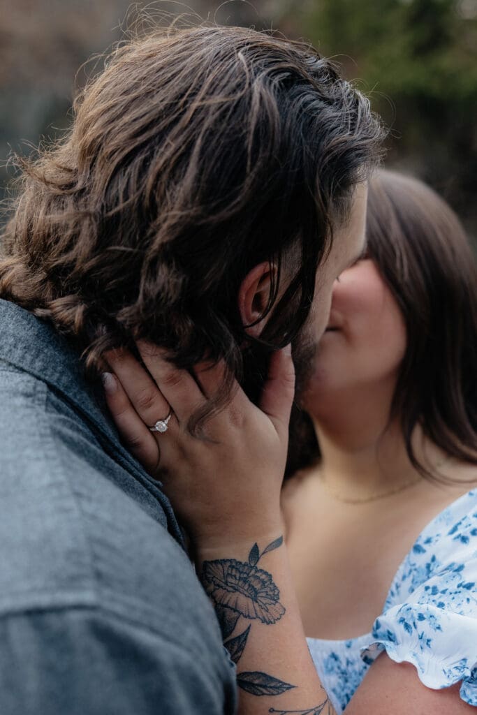 Close-up of an engaged couple kissing, showcasing the engagement ring on her hand during their Duluth engagement session.