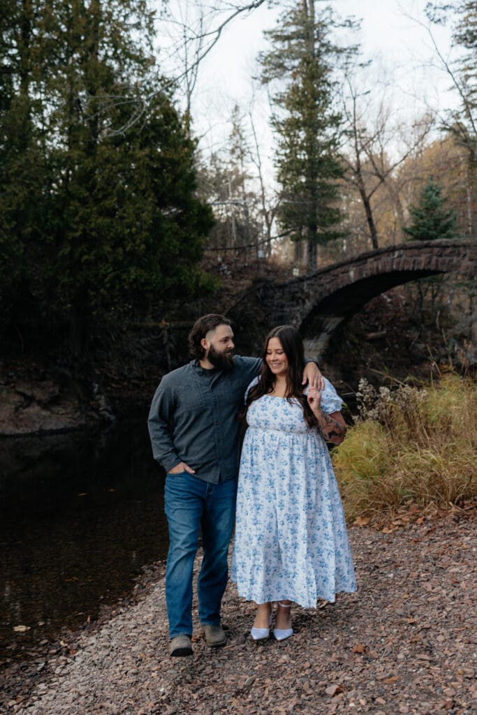 Engaged couple smiling together near a stone bridge at Glensheen Mansion in Duluth, Minnesota.