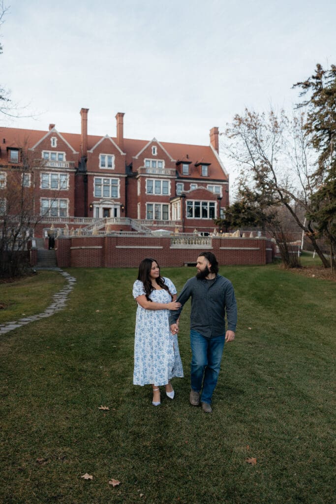 Couple walking hand in hand on the lawn of Glensheen Mansion during their Duluth Minnesota engagement session.