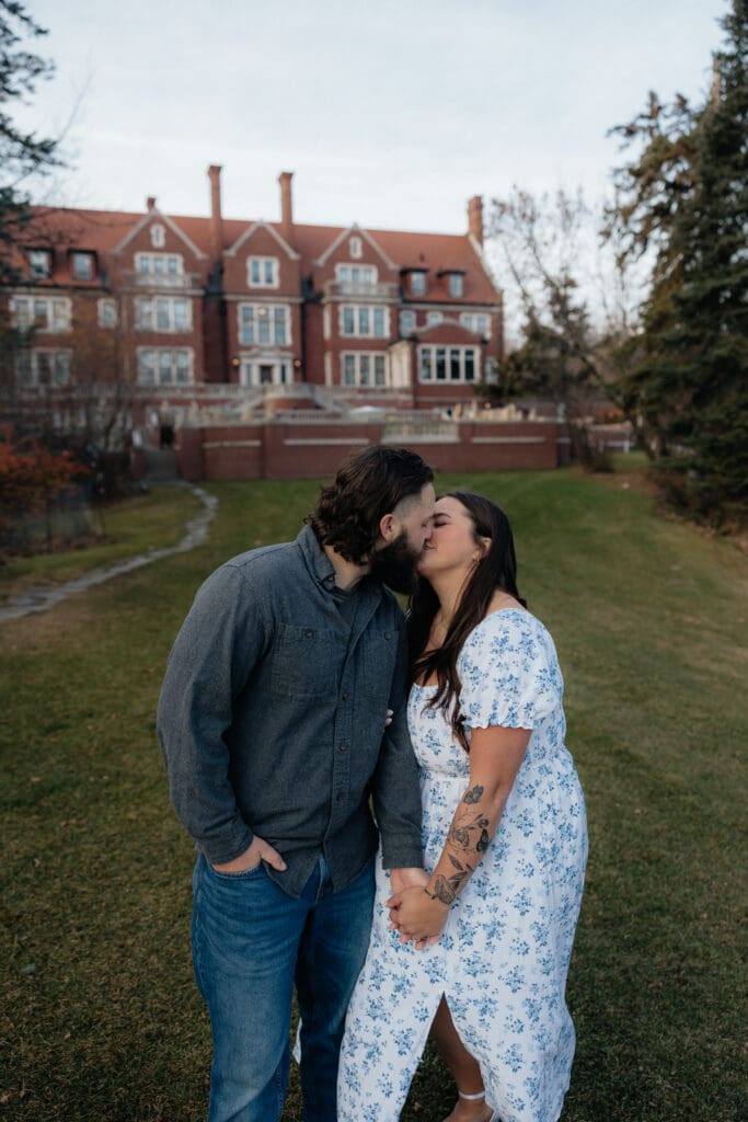 Engaged couple sharing a kiss with the historic Glensheen Mansion as a backdrop in Duluth, Minnesota.