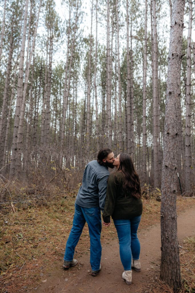 Couple walking hand in hand along a wooded trail, surrounded by tall pines in Duluth, Minnesota.