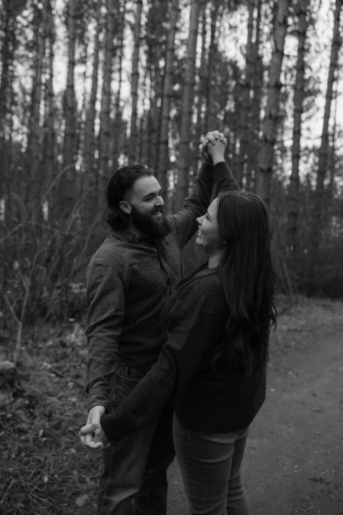 Black-and-white photo of a couple dancing on a forest trail during their engagement session in Duluth, MN.