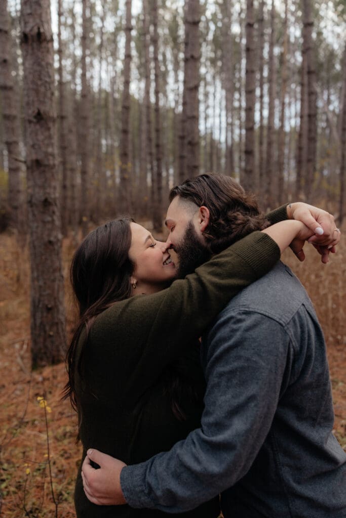 Engaged couple sharing a passionate kiss in a pine forest near Duluth, Minnesota.