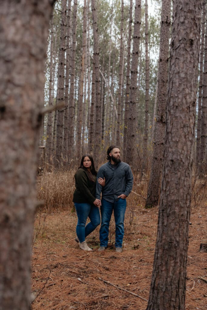 Engaged couple standing close together between the towering trees of a Minnesota forest.